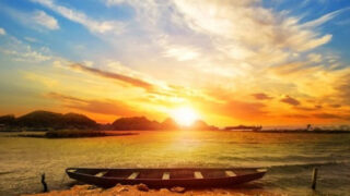 夕日の海にたたずむ一艘の小舟と、静かに広がる空と水面